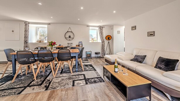 Ein modernes Wohnzimmer mit einer Couch, einem Esstisch mit Stühlen, einem Couchtisch und einem kleinen Beistelltisch.