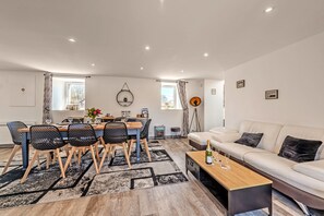 A modern living room with a sofa, a dining table with chairs, a coffee table, and a small side table.