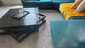 Una sala de estar con una mesa de centro de madera oscura, un sofá color turquesa y una manta amarilla.