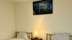 Una habitación con dos camas individuales, una mesita de noche con lámpara y un cuadro de un puente.