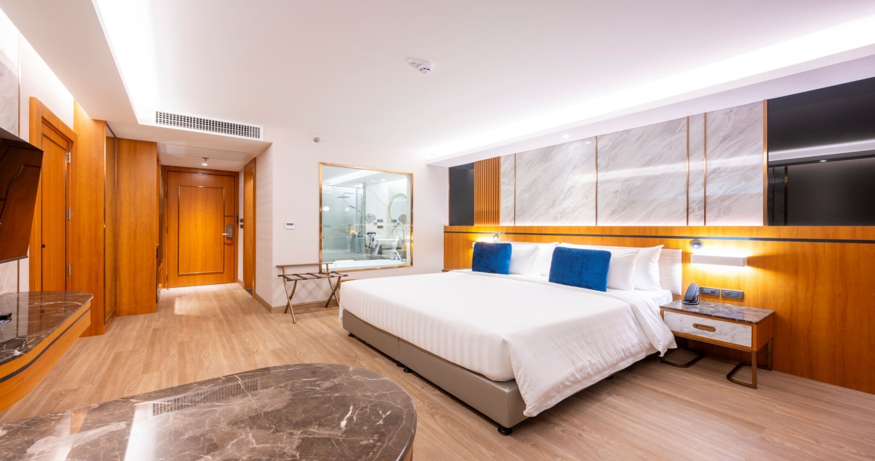 A modern hotel room with a large bed, wooden flooring, a marble table, and a large window.