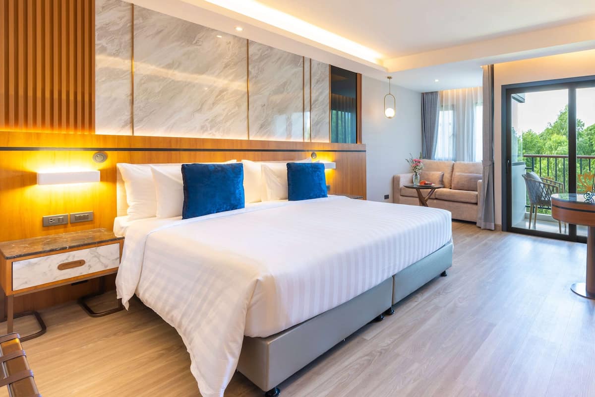 Moderni hotellihuone, jossa on suuri sänky, puiset yöpöydät, marmorilla koristeltu seinä ja parveke, jolta on näkymä.