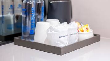 A tray with bottled water, a white mug, and a white container with snacks.