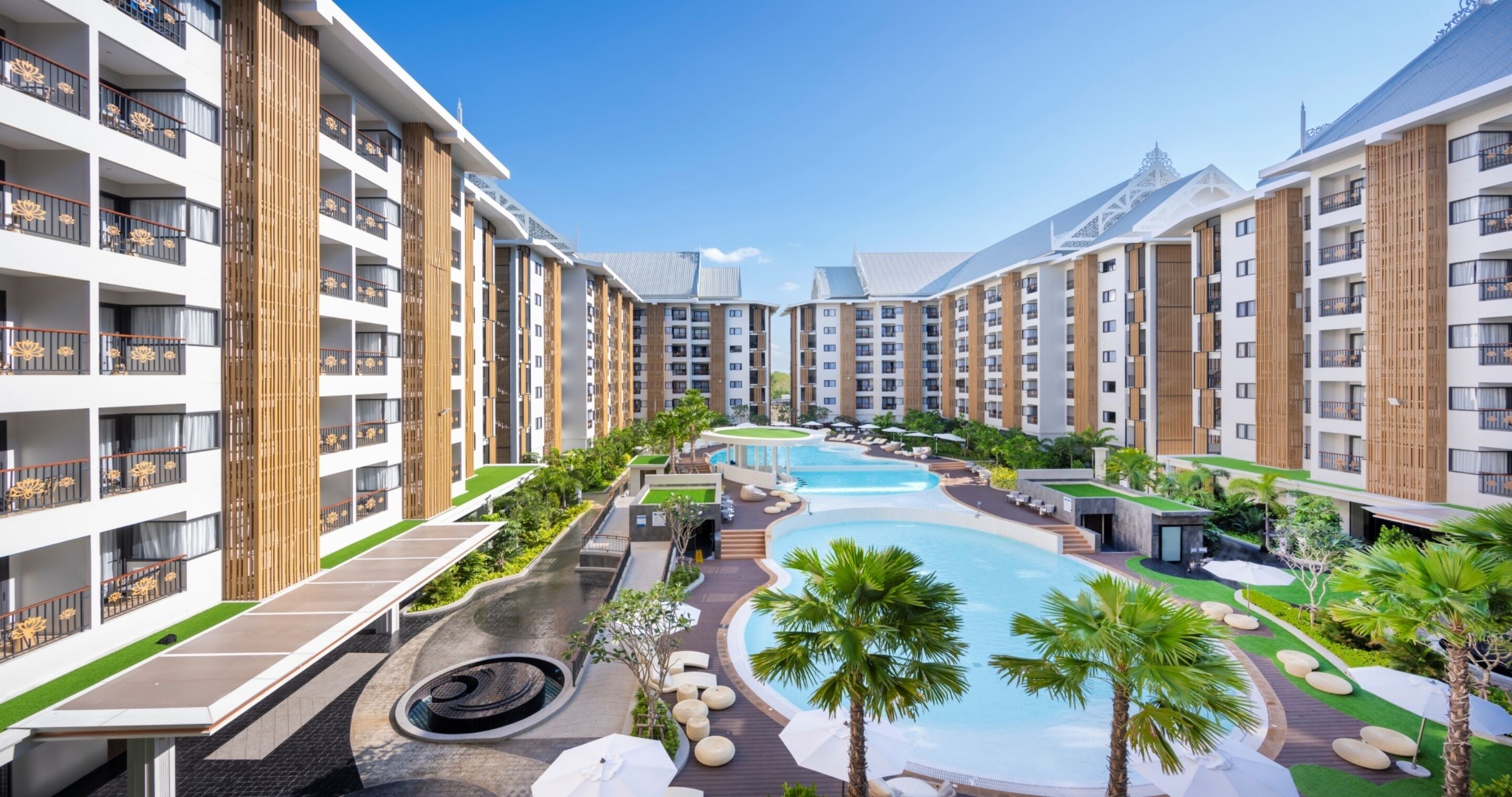 A modern hotel with multiple floors, a central swimming pool, and outdoor seating areas.