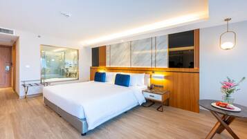 A modern hotel room with a large bed, bedside tables, a mirror, a small table with a vase, and a wooden floor.