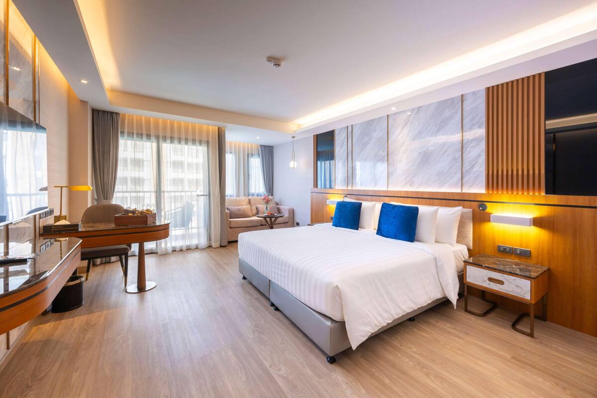 A modern hotel room with a large bed, a desk, a chair, and a TV.