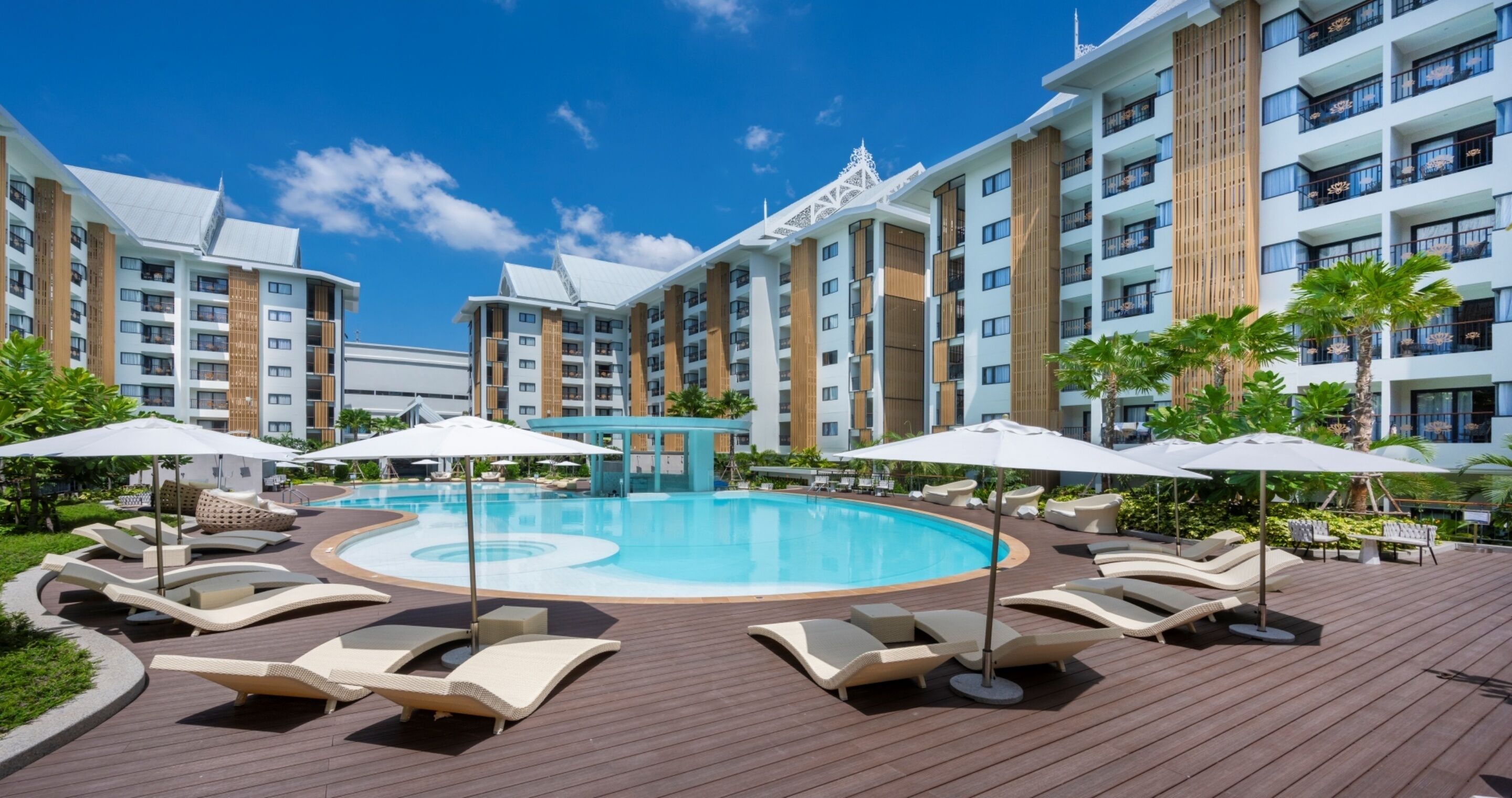 A resort with a central swimming pool, lounge chairs, and umbrellas.