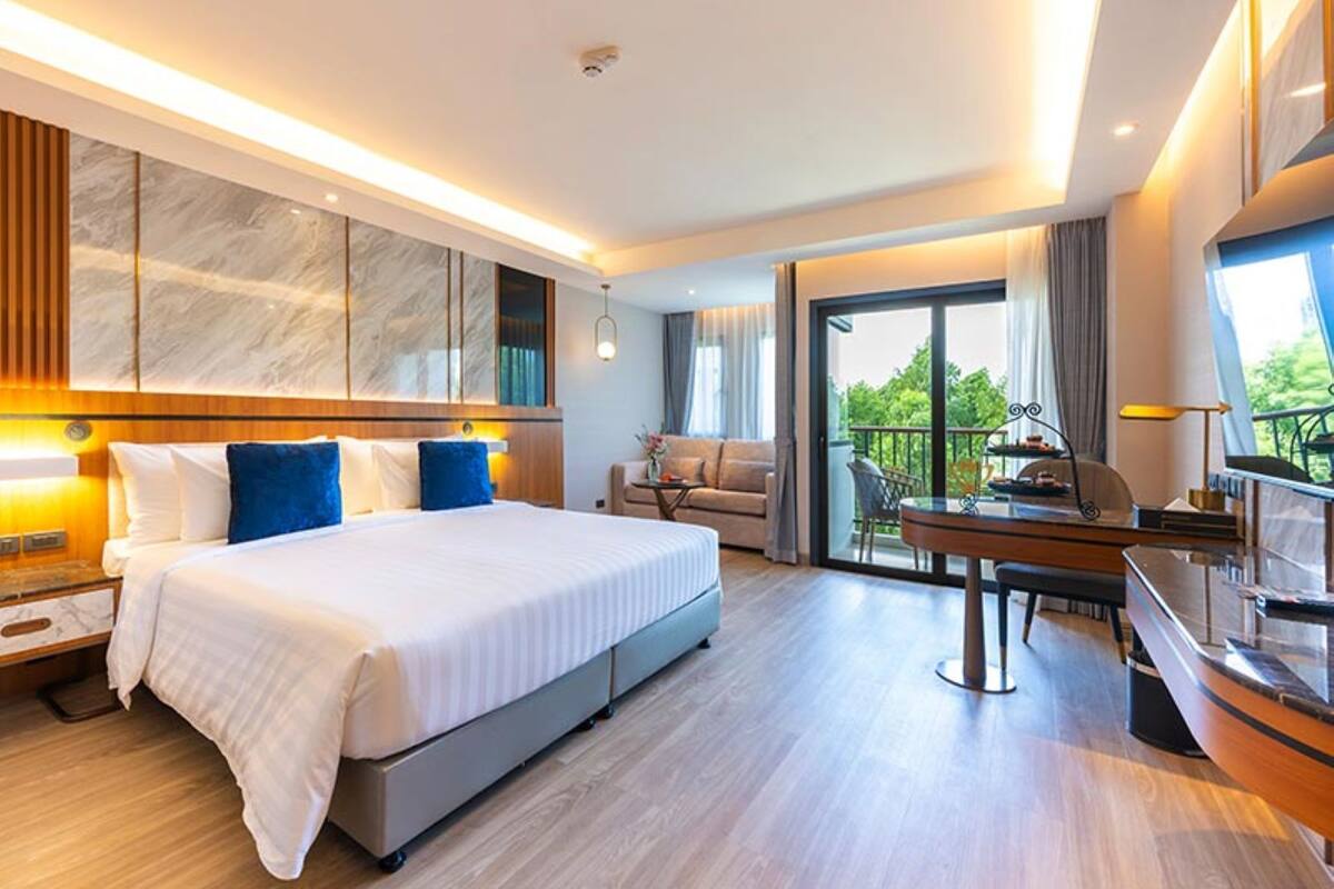 A modern hotel room with a large bed, a desk, and a balcony with a view.