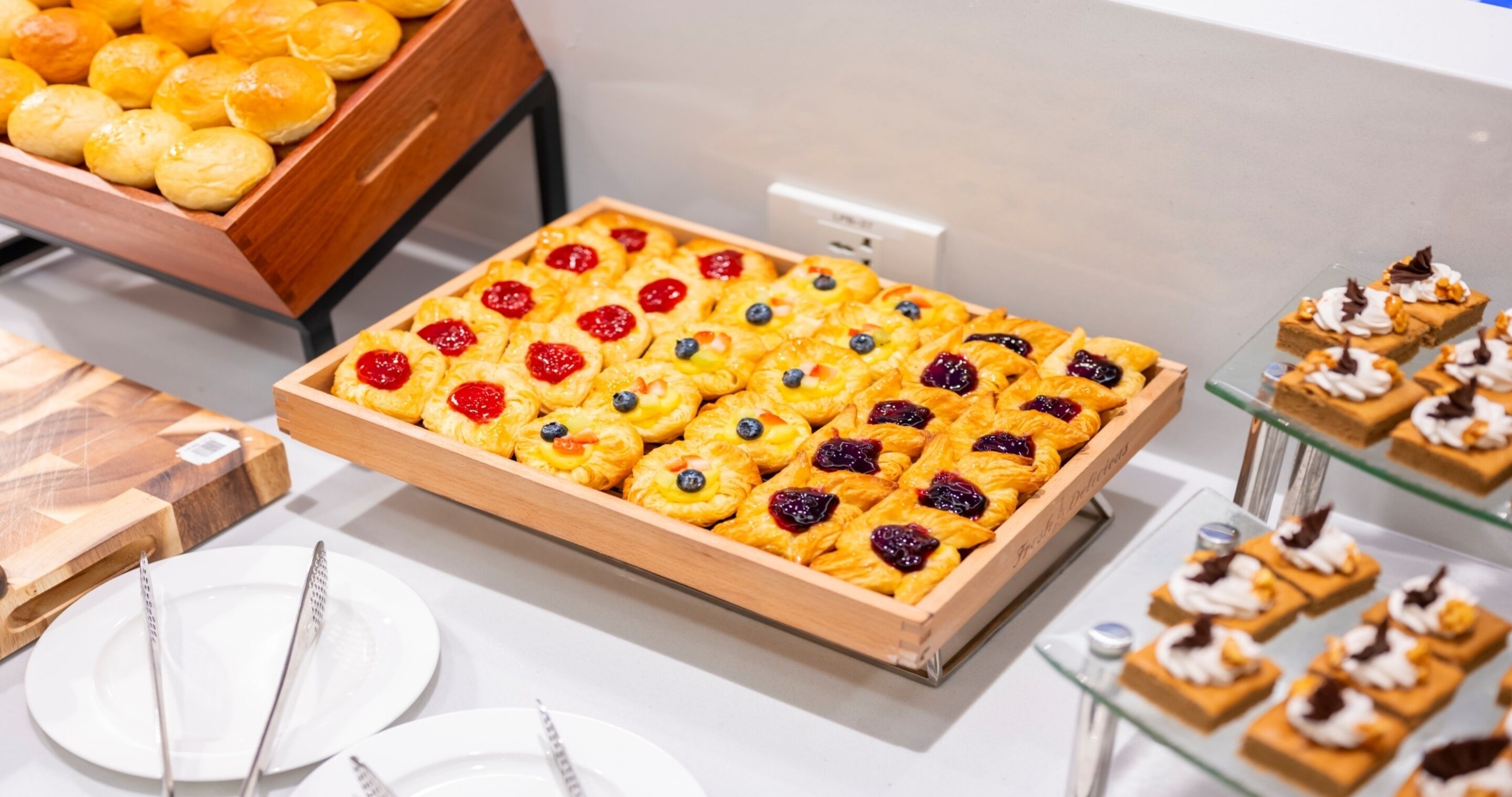 Un plateau de viennoiseries aux fruits rouges et une boîte en bois contenant des petits pains.