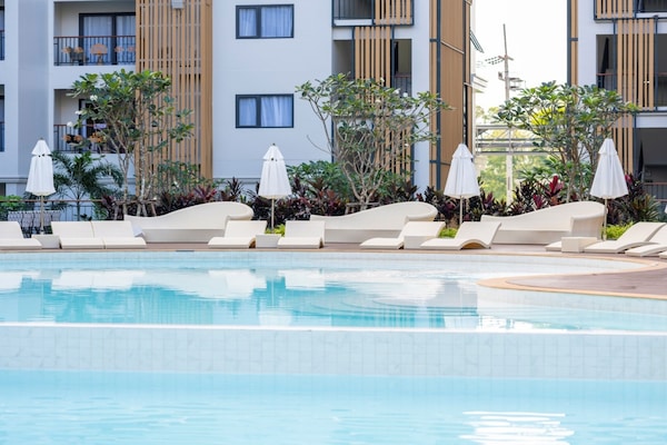 Una piscina al aire libre, sombrillas, sillones reclinables de piscina