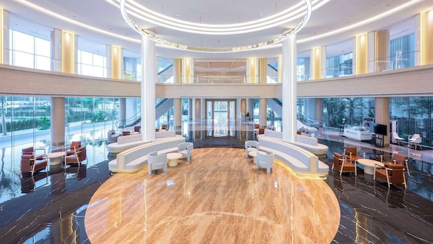 Un vestíbulo amplio con una zona de estar circular, ventanas grandes y un techo alto con una lámpara circular.