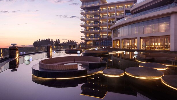 Um hotel moderno com área de piscina no terraço, assentos circulares e fachada de vidro.