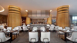 Um restaurante moderno com um bar central, cadeiras brancas e luminárias cilíndricas.