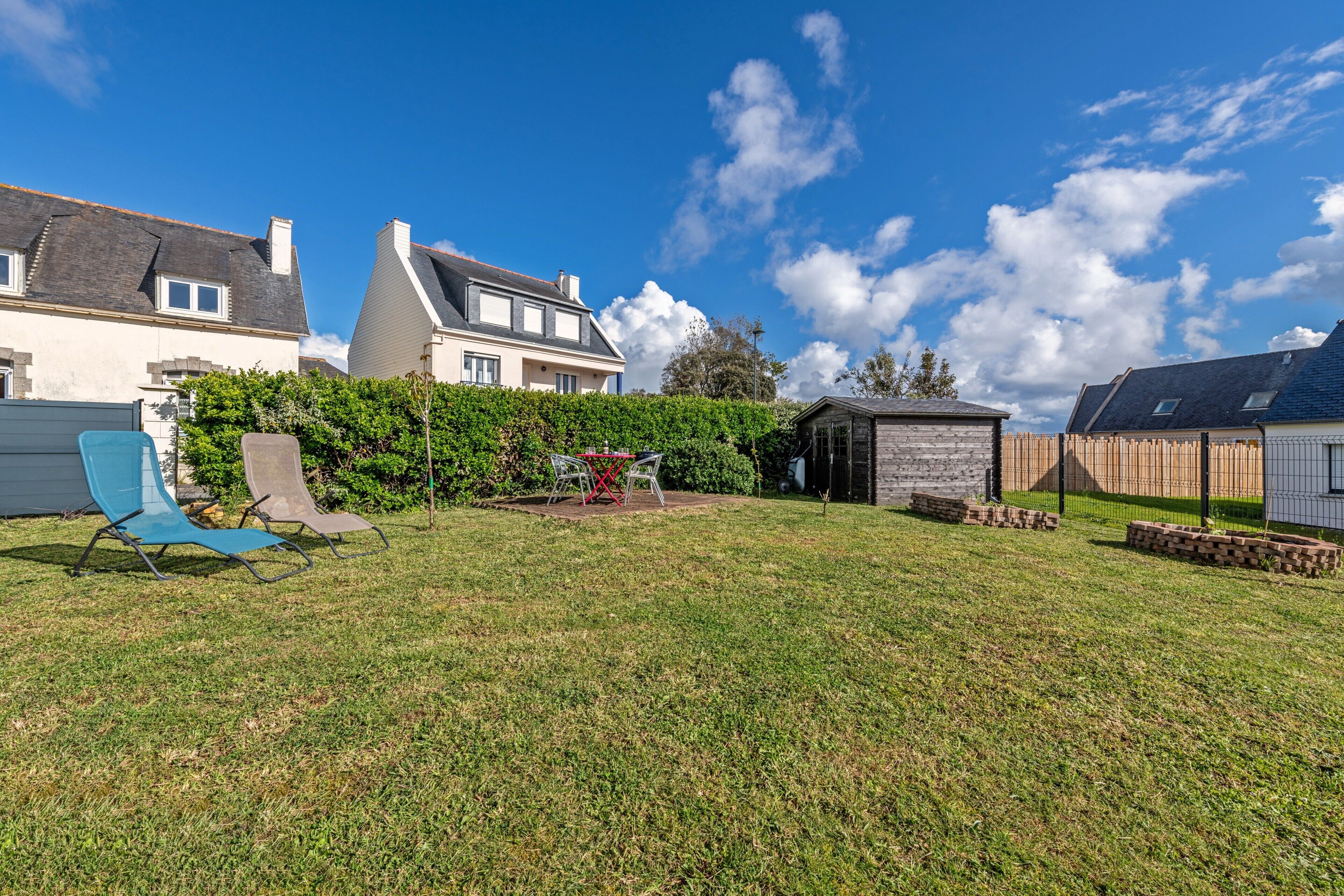 Ein Garten mit Rasen, einer kleinen Gartenhütte und einem blauen Stuhl.