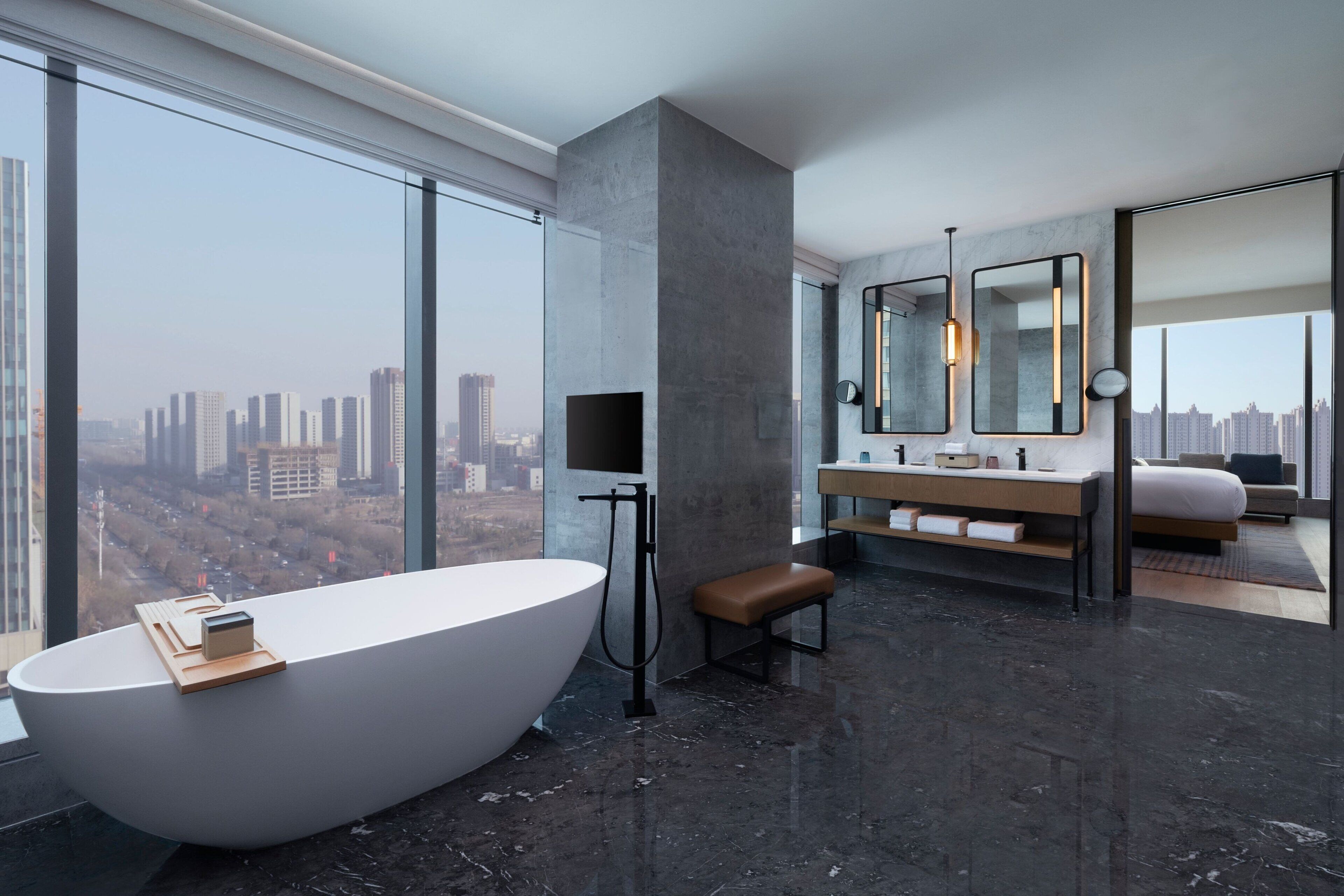 A modern bathroom with a freestanding bathtub, a large mirror, and a city view.
