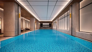 A long, narrow indoor swimming pool with tiled walls and ceiling, flanked by seating areas and a staircase leading to upper levels. - Sheraton Taiyuan (Taiyuan)