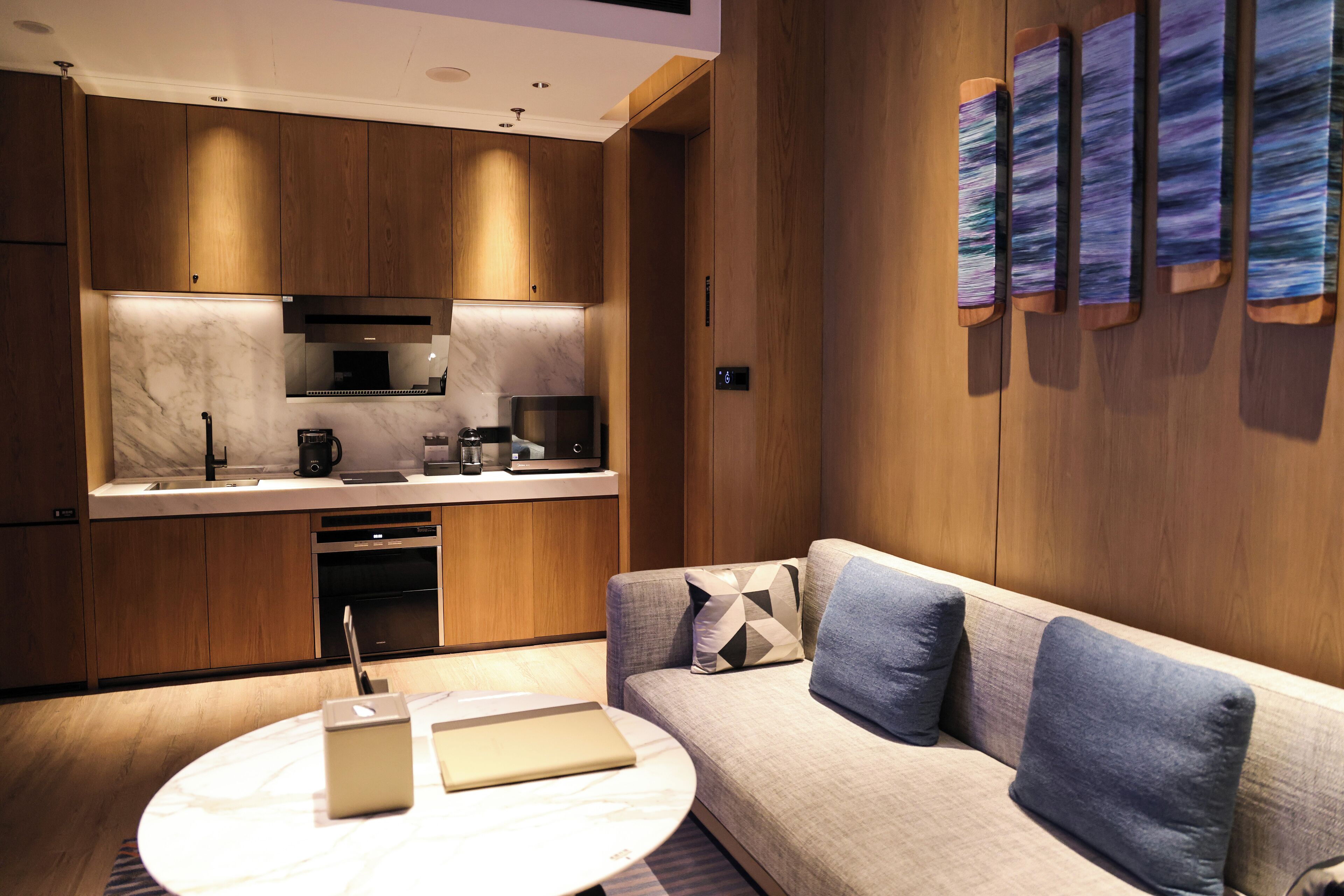 A modern kitchen with wooden cabinets and a marble countertop, a built-in oven, and a coffee machine.