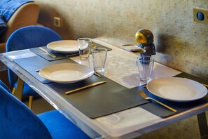 Een eettafel gedekt met borden, bestek en glazen, met een blauwe stoel op de achtergrond.