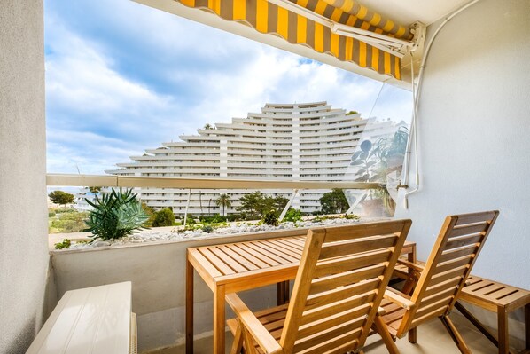 A balcony with a wooden table and chairs, a view of a modern building, and a clear sky.