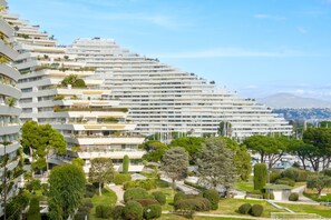 Een modern meerlaags hotel met balkons, een aangelegde tuin en uitzicht op zee en bergen.