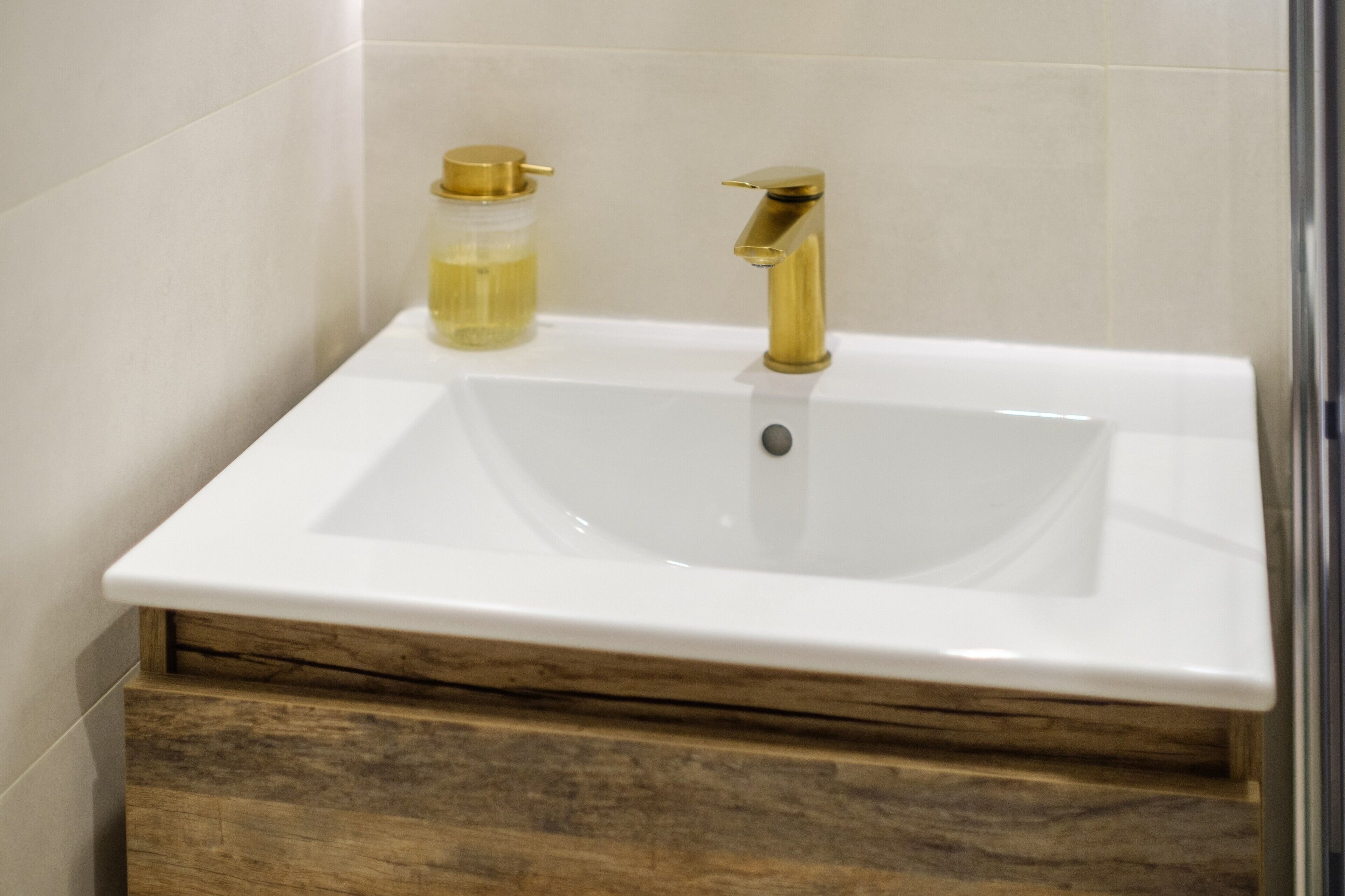 Ein Badezimmer mit einem weißen Waschbecken, einem goldenen Wasserhahn und einer Holzausstattung.