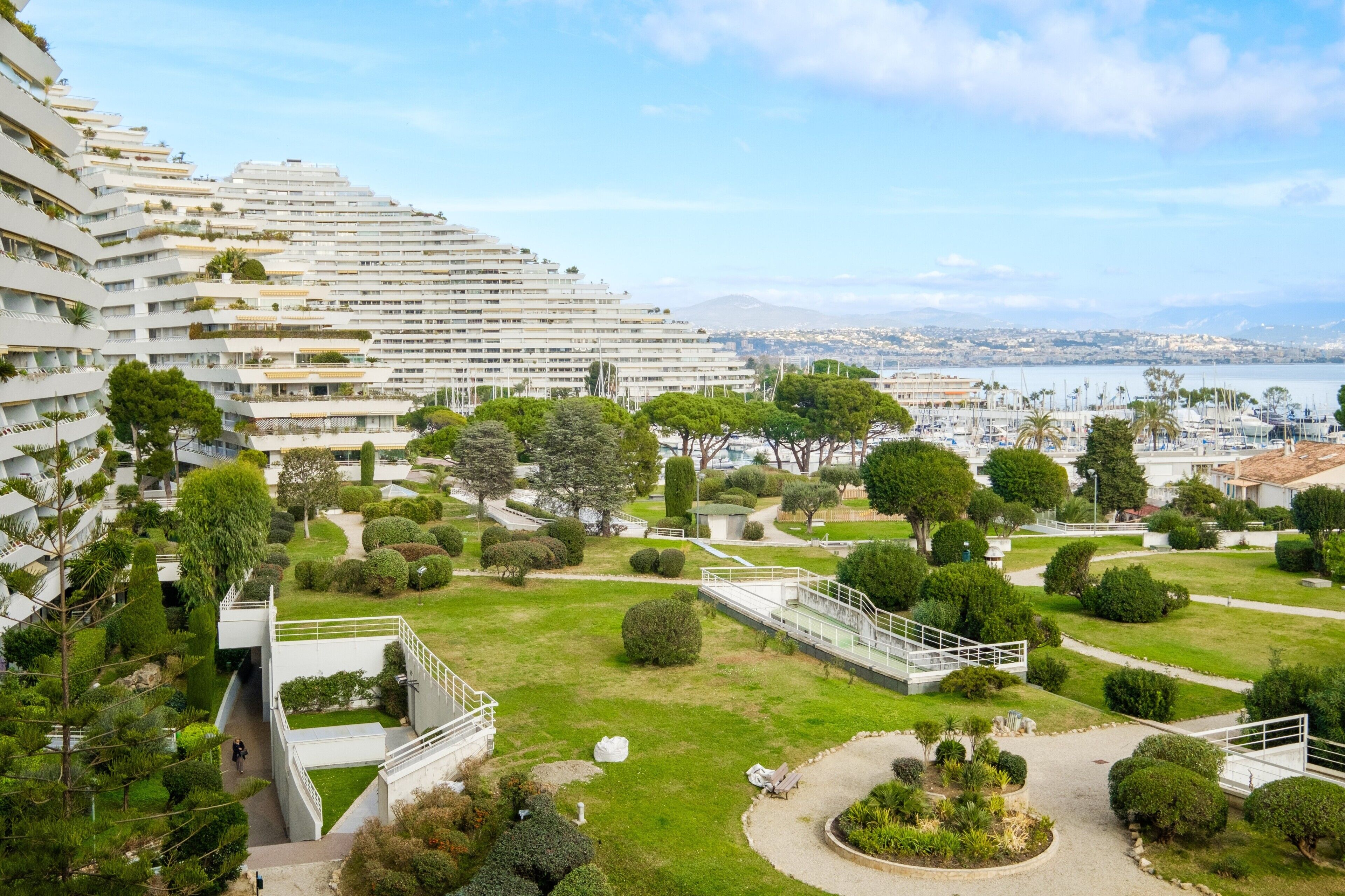 A modern hotel with a landscaped garden, a marina in the background, and a view of the city.