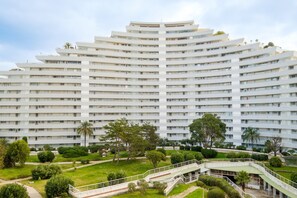 A multi-story hotel with a curved facade, multiple balconies, and a landscaped garden with pathways and trees.