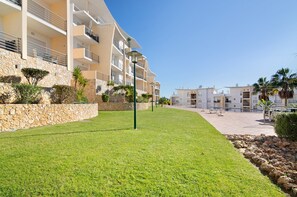 A modern hotel with a stone retaining wall, a well-maintained lawn, and a clear sky.