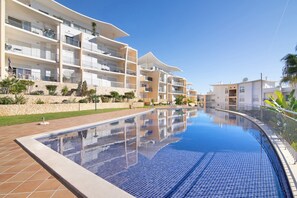Et moderne hotel med swimmingpool, altaner og en stenvæg.