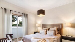 Habitación de hotel con una cama grande, dos mesitas de noche, una silla y vistas a través de una puerta corrediza de vidrio.