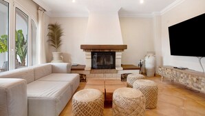 A living room with a fireplace, sofa, ottomans, and a television. - La Casita del Mar – House with Jacuzzi, Garden & Terraces 300 m from the Beach in Torremolinos (Torremolinos)