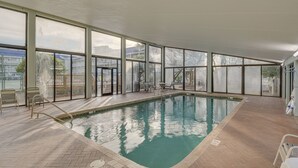 Una piscina coperta con pareti in vetro trasparente, pavimento piastrellato e scaletta.