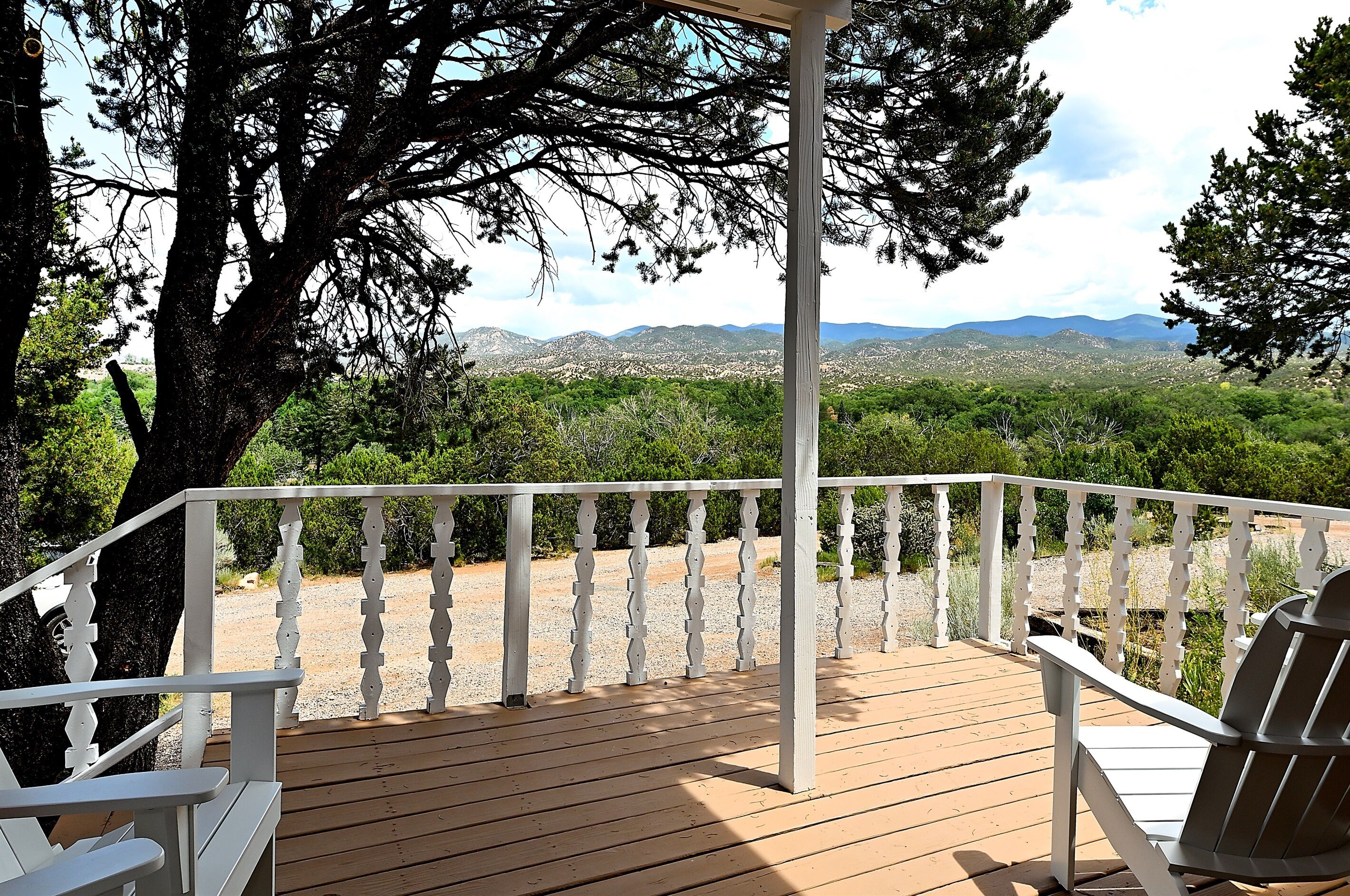 A wooden deck with white railings, a covered seating area, and a view of a mountainous landscape.