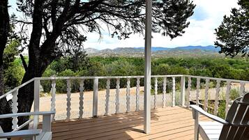 A wooden deck with white railings, a covered seating area, and a view of a mountainous landscape.
