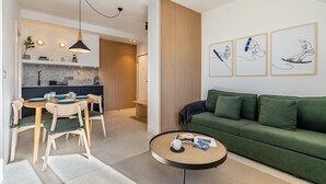 Moderni olohuone, jossa on vihreä sohva, pyöreä sohvapöytä ja ruokailutila, jossa on puinen pöytä ja tuolit.