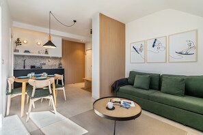 Un saló modern amb un sofà verd, una taula de centre rodona i una zona de menjador amb una taula i cadires de fusta.