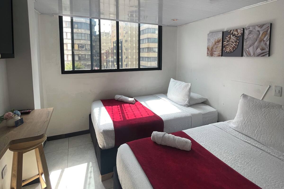 Habitación de hotel con dos camas, un escritorio y ventana con vista a la ciudad.