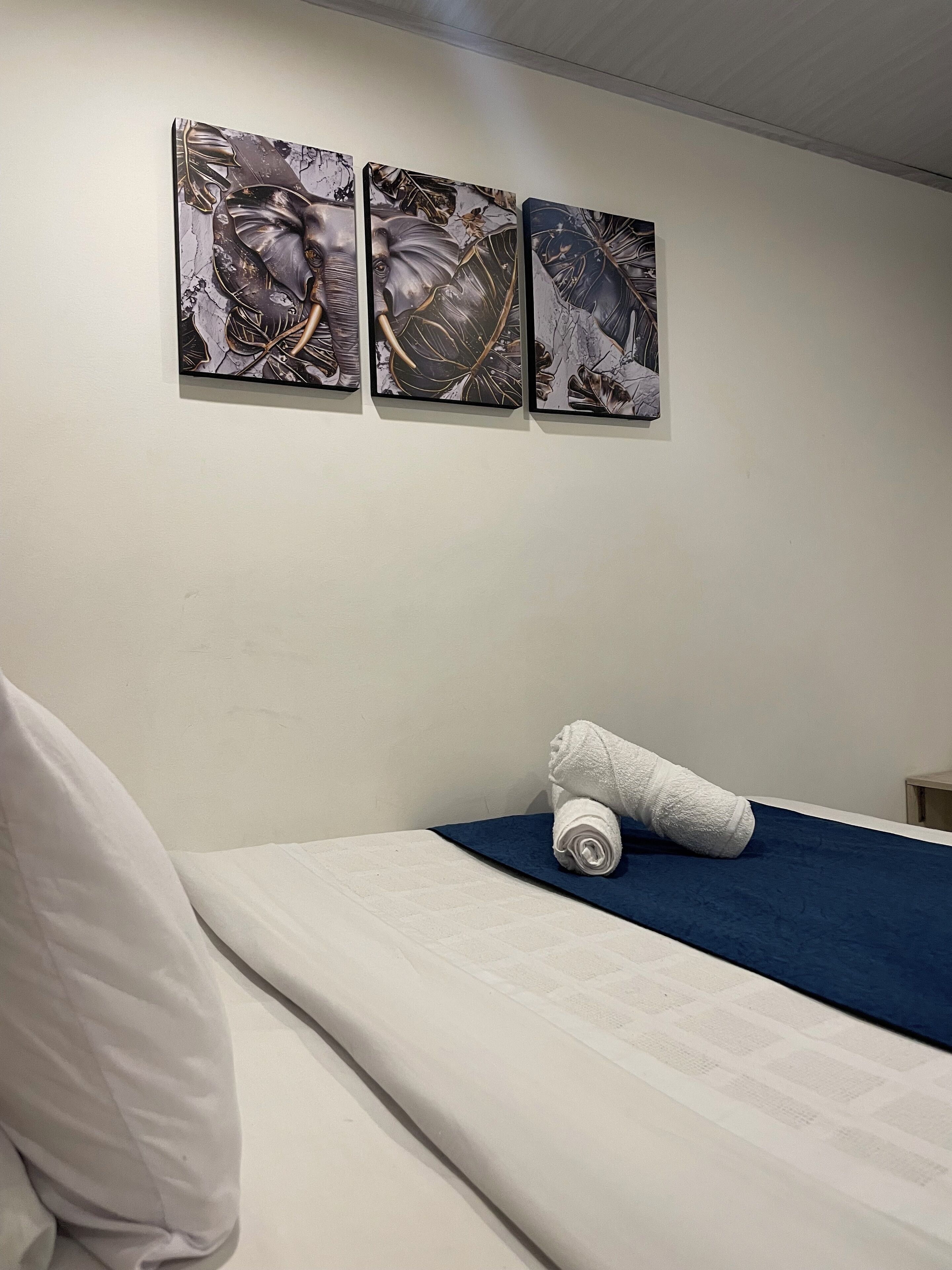 Una habitación de hotel con una cama, un almohadón y tres obras de arte enmarcadas en la pared.
