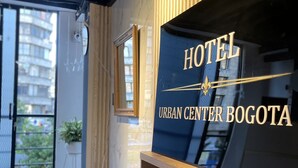Un interior de hotel moderno con un espejo grande, una barra de madera y un cartel que dice 'HOTEL URBAN CENTER BOGOTA'.