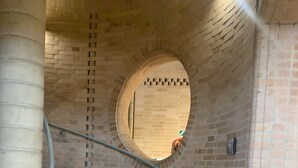 Una escalera de caracol con escalones de madera y barandillas metálicas, que conduce a un muro de ladrillo con un ventanal circular.