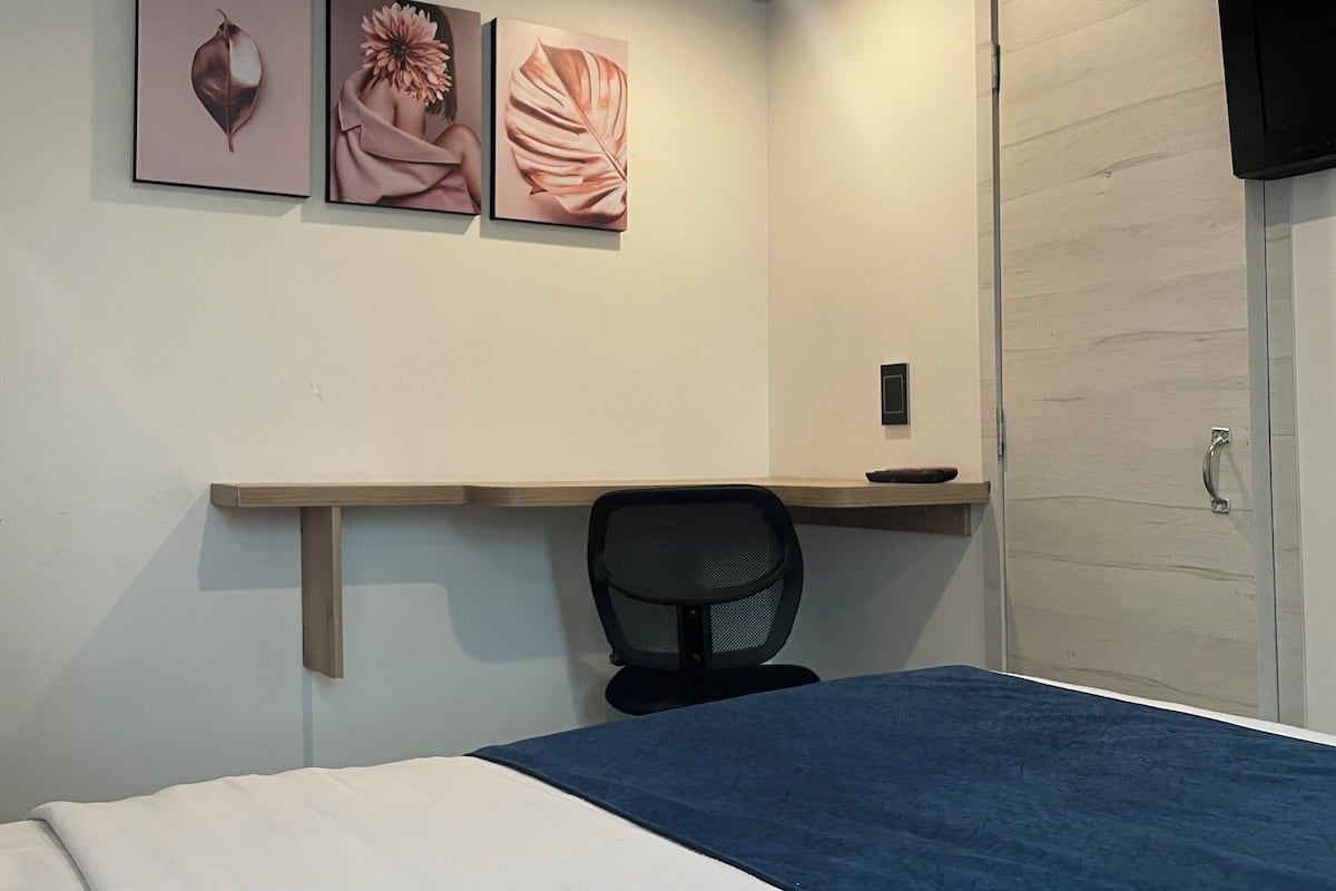 Un dormitorio con una cama, un escritorio y una silla. Hay tres cuadros en la pared.