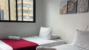Habitación de hotel con dos camas, cada una con una colcha blanca y roja, y una ventana con vistas a edificios.