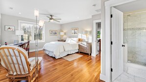 A bedroom with a bed, bedside tables, a chair, a desk, a ceiling fan, and a shower area. - Modern Family Home Walkable to Town (Tisbury)
