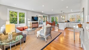 A spacious living area with a sofa, coffee table, and a television. There is a kitchen area with a dining table and chairs. - Modern Family Home Walkable to Town (Tisbury)