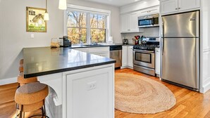 A modern kitchen with white cabinetry, stainless steel appliances, and a central island. - Modern Family Home Walkable to Town (Tisbury)
