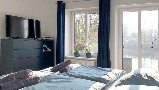 A bedroom with a bed, a dresser, a TV, and a window with curtains. - Schleusenhaus in Hameln (Hameln)