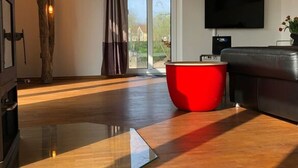 A modern living room with a wooden floor, a glass coffee table, a red ottoman, a black leather sofa, and a flat-screen TV mounted on the wall. - Schleusenhaus in Hameln (Hameln)
