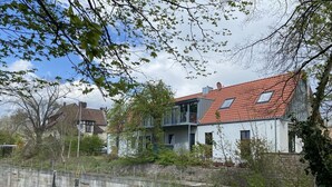 A residential area with houses featuring red-tiled roofs and a stone wall running parallel to a body of water. - Schleusenhaus in Hameln (Hameln)