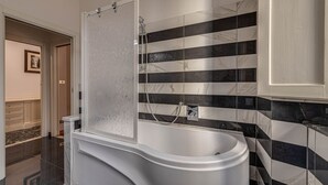Een moderne badkamer met een vrijstaand bad, een douchecabine en een betegelde wand met een marmer dessin.