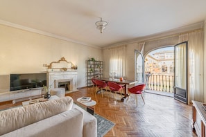 A living room with a sofa, TV, fireplace, dining table with chairs, and a balcony with a view of buildings. - Apartments Florence- Golden Tower with View (firenze)